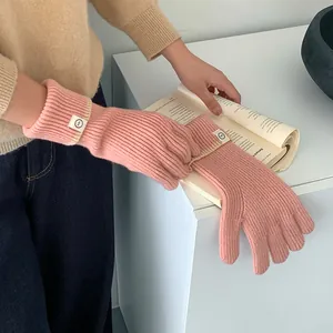 Close-up of pink knitted gloves featuring cream contrast cuffs and decorative woven labels
