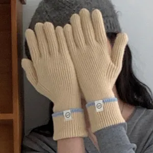 Close-up detail of beige knitted gloves with contrast blue trim and circular label