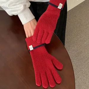 Close-up of stylish red knitted winter gloves featuring navy stripes and a white patch