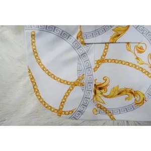 Détail de chaînes baroques dorées et motifs méandres sur tissu de blazer blanc élégant.