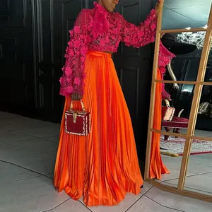 Vibrant orange pleated maxi skirt paired with a magenta 3D floral lace top in a studio setting.