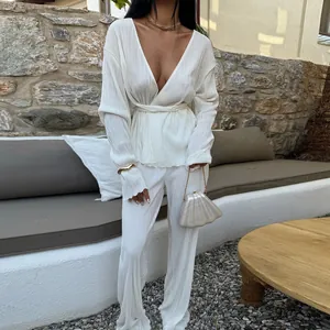 Elegant white pleated two-piece set featuring long sleeve V-neck top and matching trousers.