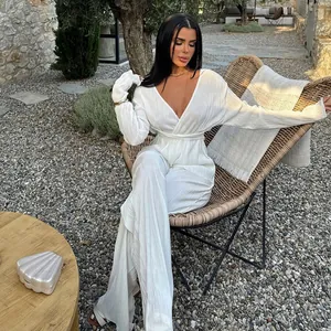 Elegant white pleated long sleeve jumpsuit with deep V-neck in outdoor resort setting