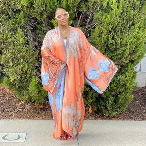 Full-length view of a women's loose orange floral print kimono cardigan outdoors.