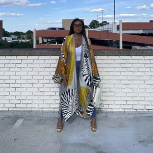 Street style view of a woman in a long printed kimono coat against a white brick wall