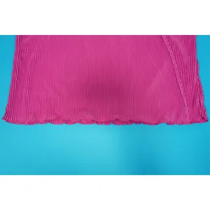 Detailed close-up view of pink pleated fabric with a lettuce edge hem on a blue surface
