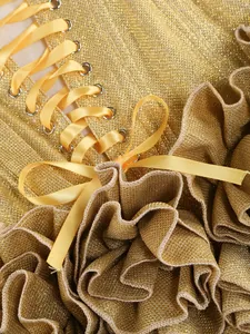 Close-up of gold sequined dress with yellow lace-up ribbon and ruffled detail.