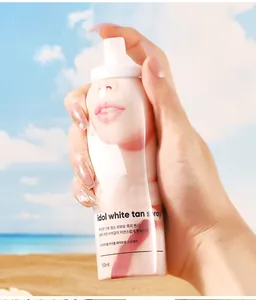 Dettaglio del flacone Idol White Tan Spray tenuto in mano con sfondo di spiaggia