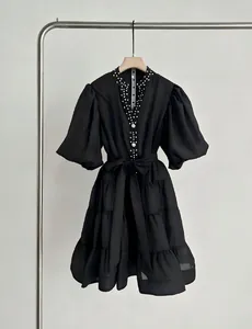 Detalle de vestido negro de capas con cuello en V, mangas abullonadas y pedrería.