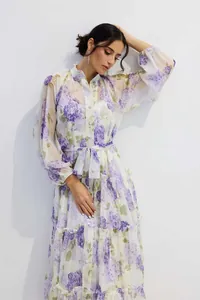 Detail of elegant white floral chiffon dress featuring purple blooms and lantern sleeves.
