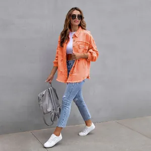 Vibrant orange loose ripped denim jacket for women walking against a textured grey wall