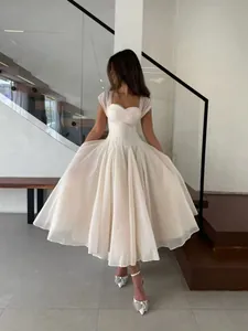 Full-length view of a white pleated dress with sheer cap sleeves worn by a model.