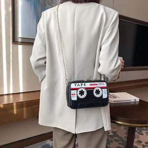 Fashionable black cassette tape shaped crossbody bag with gold chain strap shown on model