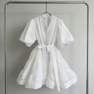 Elegante minivestido blanco con volantes, mangas farol, lazo en la cintura y pedrería