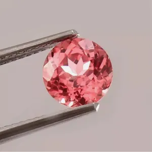 Macro de un zafiro Padparadscha de corte redondo sostenido por pinzas de precisión.