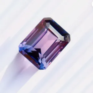 Detail of an emerald-cut blue-purple sapphire gemstone with sharp facets and gradient.