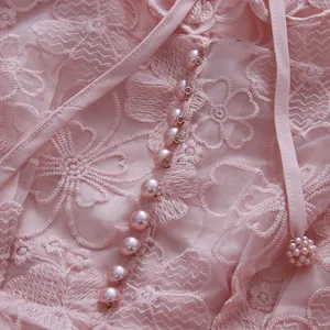 Detailed view of pink lace dress featuring intricate floral embroidery and pearl buttons.
