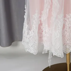 Detailed macro view of delicate white lace embroidery on the hem of a pink dress