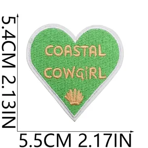 Grüner herzförmiger Stickaufnäher mit Coastal Cowgirl Text und dekorativer Muschel.