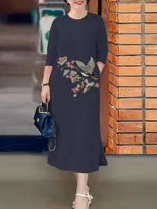 Vue détaillée de la broderie complexe d'oiseaux et de fleurs sur la robe bleu marine.