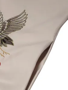 Détail en gros plan de la broderie d'aigle et de la poche latérale sur une robe beige