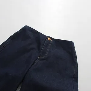 Macro detail of dark blue denim jeans waist featuring a polished golden button.