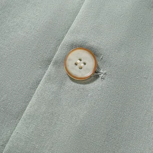 Close-up of resin button and sage green textured fabric on men's cotton linen jacket