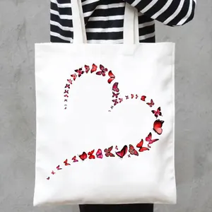 Detailed view of white canvas tote bag featuring a vibrant red butterfly heart print.