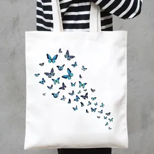 Close-up of a white canvas tote bag with blue butterfly print pattern held by a person.