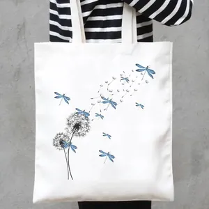 Close-up detail of a white canvas tote bag featuring a blue dragonfly and dandelion print