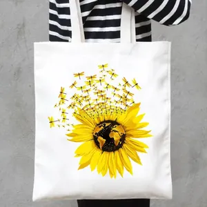 Close-up of white canvas tote bag featuring vibrant sunflower and dragonfly print detail.