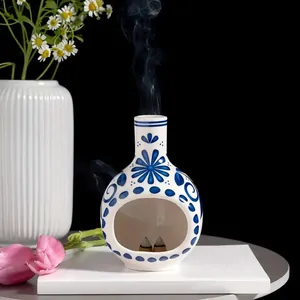 Elegante quemador de incienso de cerámica azul y blanca con humo saliendo de la chimenea