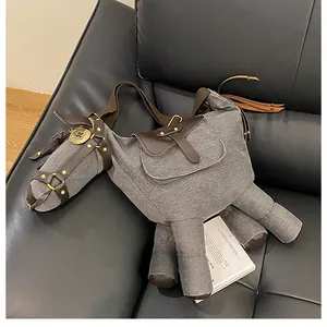 Close-up detail view of a quirky donkey-shaped canvas crossbody bag on a black leather sofa.
