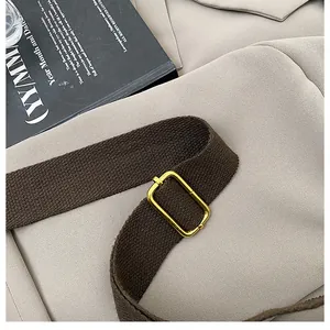Detailed shot of brown canvas strap and golden metal buckle on a beige niche bag