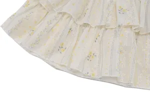 Détail en gros plan de l'ourlet à volants avec broderie florale jaune sur tissu crème