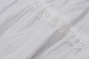 Gros plan de la délicate dentelle blanche sur le tissu froissé d'une robe de style français.