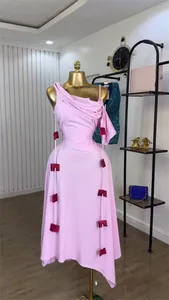 Detailed view of the light pink one-shoulder midi dress featuring dark red decorative bows