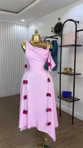 Elegant pink one-shoulder midi dress featuring decorative red bows on hanging straps