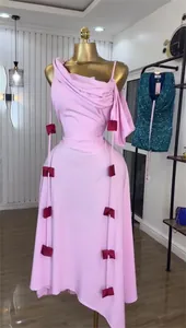 Detailed view of the elegant pink one-shoulder midi dress with dark red bow accents.