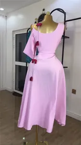 Rear view detail of elegant pink one-shoulder midi dress with red tassel accents on mannequin