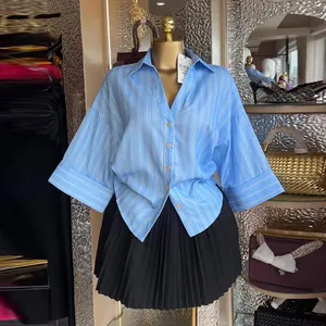 Dettaglio camicia a righe azzurre con maniche a pipistrello e colletto rovesciato.