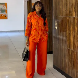 Detail view of a model in an orange printed autumn shirt and wide-leg trousers