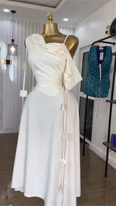 Detailed view of white asymmetrical shoulder dress with decorative hanging fabric squares