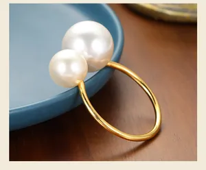Macro view of a gold finish napkin ring featuring two elegant white pearls on a wood table