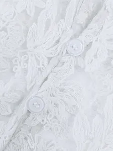 Macro detail showing intricate white floral embroidery and buttons on a lace shirt