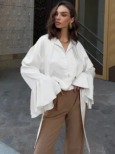 Close-up of white satin shirt with elegant floating tie and ruffled bell sleeves