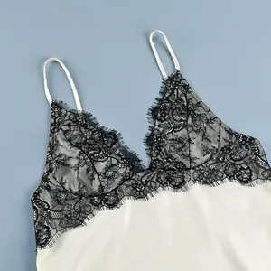 Detail view of delicate black floral lace stitching on a creamy white satin camisole top.
