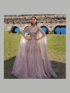 Elegant lavender sequin mesh evening gown with long cape sleeves in a scenic setting.