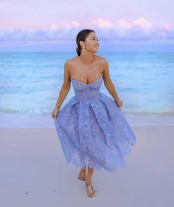 Woman wearing an elegant lavender lace strapless midi dress walking on a tropical beach at sunset