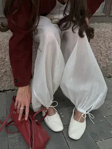 Detail of white semi-sheer loose trousers with drawstring cuffs and ballet shoes